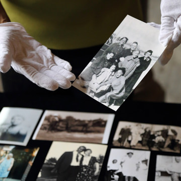 Person holds picture from family photographic archive; other photos lay on the table in front them