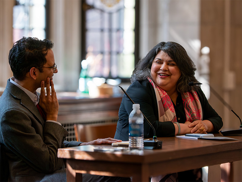 Sunil Amrith and Sharmila Sen sitting at a desk, engaged in conversation and smiling.