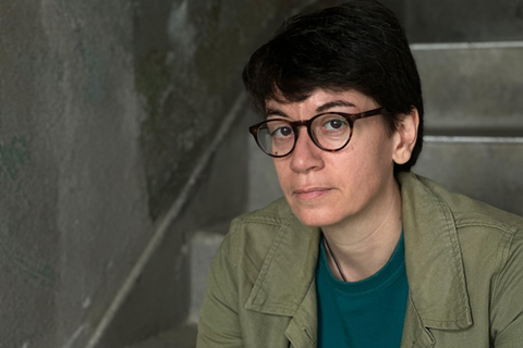 Courtesy of Eve Sussman Headshot of Samira Negrouche, sitting in a stairwell, staring directly into the camera.