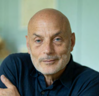 Portrait of a man with a short beard resting his chin on his hand, looking at the camera.